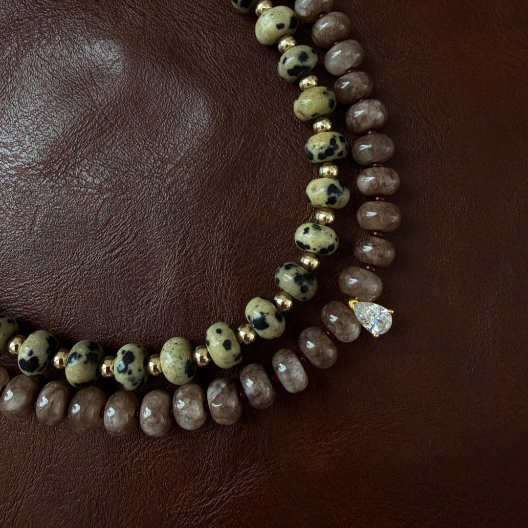 Společný detail náhrdelníků Sienna Drop Necklace a Dune Necklace na hnědém pozadí